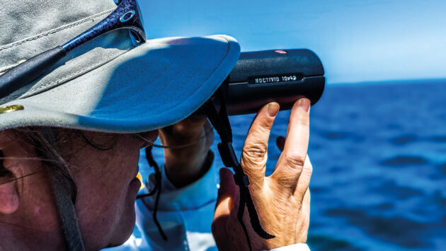 A man using binoculars for pilotage on a boat