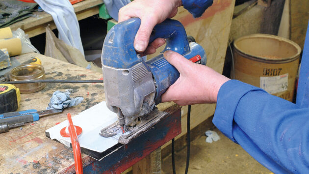 A man using a jigsaw cutting tool to make a perspex switch panel for a boat