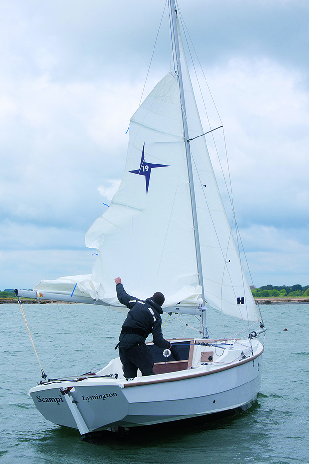 A man hoisting a mainsail on a small boat