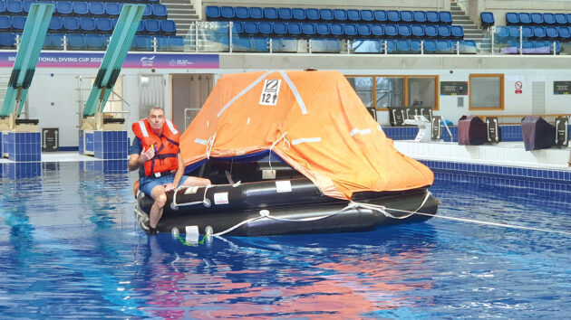 A man wearing a lifejacket sitting on the edge of a liferaft while practising sea survival and how to survive if lost at sea