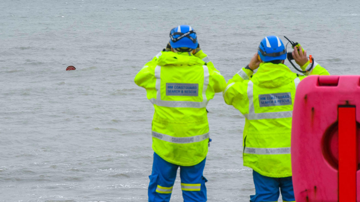 An HM Coastguard search and rescue team keeping watch on a large wooden cable reel floating 100 meters off the beach at Burton Bradstock, Dorset. Credit: Graham Hunt/Alamy