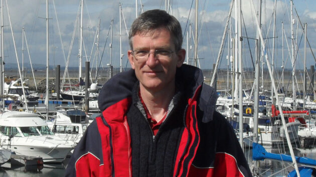 A skipper wearing glasses and a red and black sailing jacket