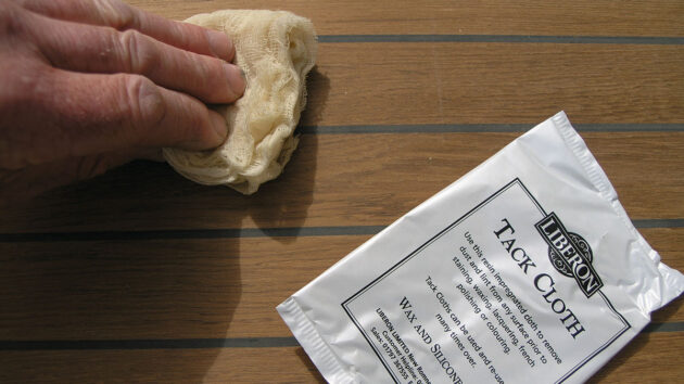 A man using a tack cloth to collect fine dust before marine varnishing wood on a boat