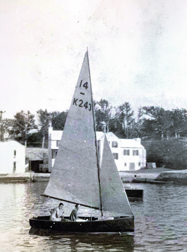 A black and white photo of a couple sailing a wooden International 14 dinghy