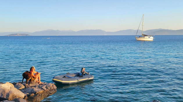 A woman sitting on rocks next to an inflatable dinghy