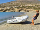 A man wearing a black tshirt and denim shorts pulling a PVC dinghy up a beach