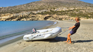 A man wearing a black tshirt and denim shorts pulling a PVC dinghy up a beach