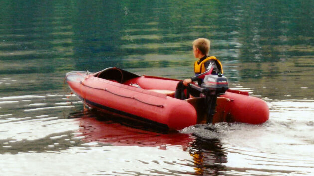 A boy manoeuvring a Tinker dinghy with an outboard engine