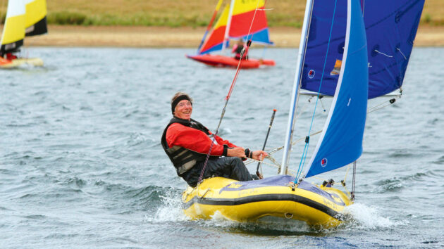 A man sailing a Tinker dinghy with a smiles on his face