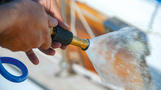 A person using a hose to clean a boat hull