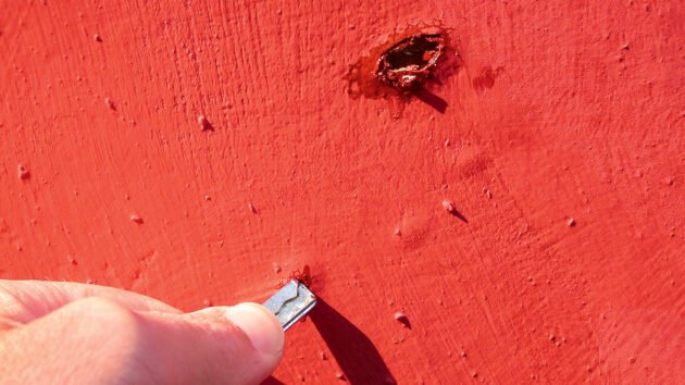 A man using a pin to check for osmosis blisters on the hull of a boat