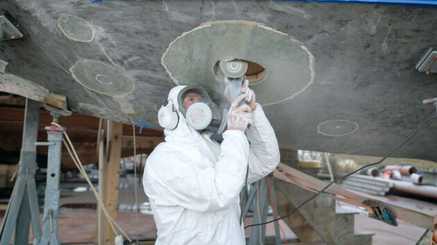 A man wearing PPE using a saw to cut a hole in the hull of an electric sailboat