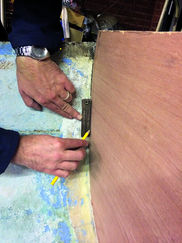 A man using a pencil to shape the hull of a boat to a bulkhead