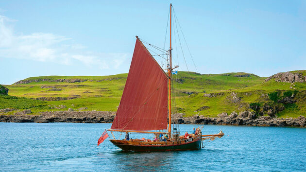 A yacht with red sails with guests on board during UK boating holidays