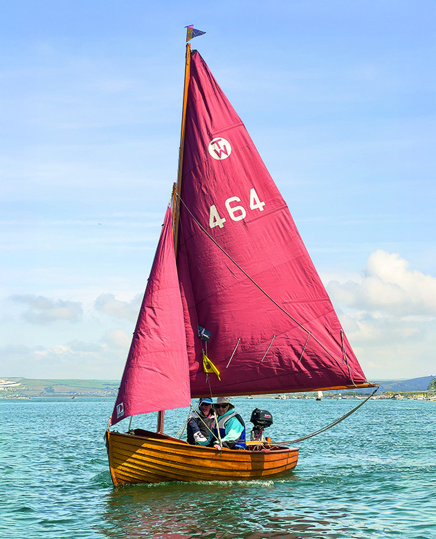 A Tideway 12 cruising dinghy sailing with a red sail