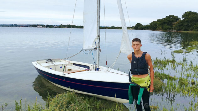 A boy standing by a Wayfarer cruising dinghy