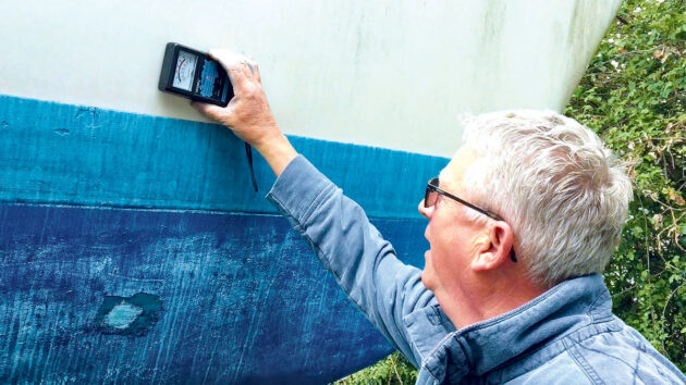A man using a moisture meter on the side of a boat