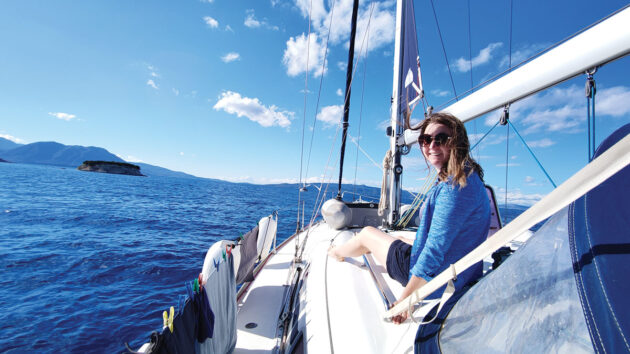 Laura Hodgetts on the bow of Bavaria 39 cruiser, Orestis charter yacht, on the Ionian Sea, during a Sail and Stay charter with Seafarer Holidays