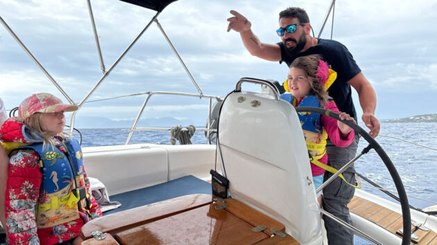 Girl at the helm of a charter yacht with a skipper supervising