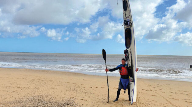 Ian Hayward with his sea kayak on a beach. Credit: timbrookphotography.pixieset.com