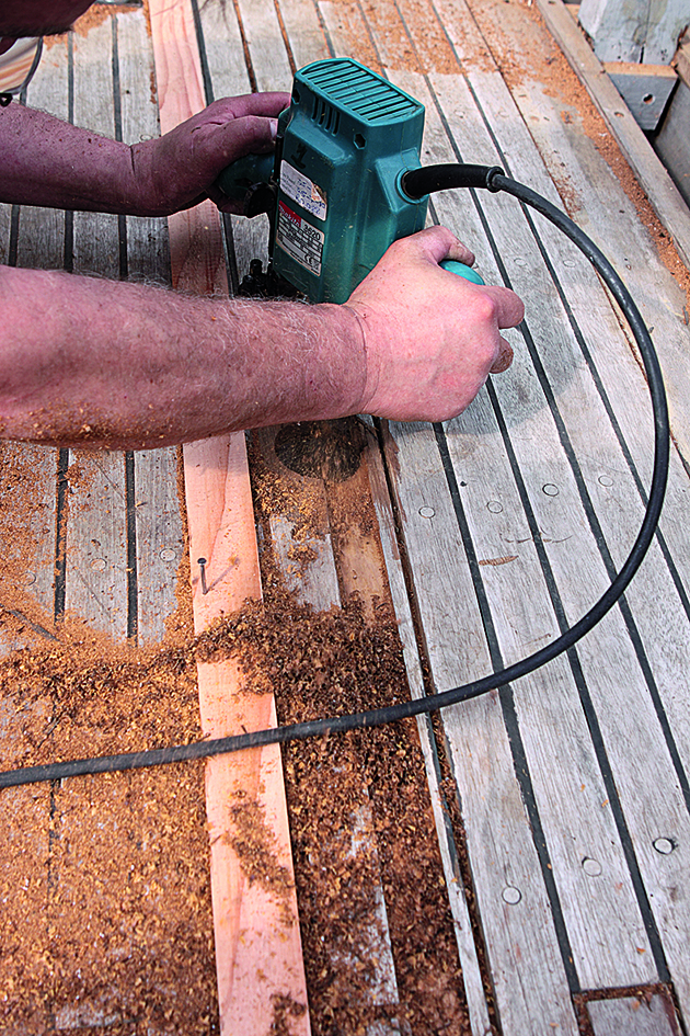 A man using a router to cut away a plank on a teak deck