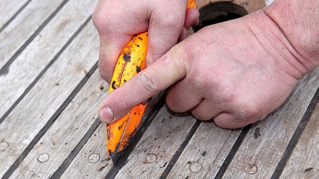A man using a craft knife to remove caulking from a teak deck