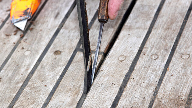 A person removing old caulking from a teak deck