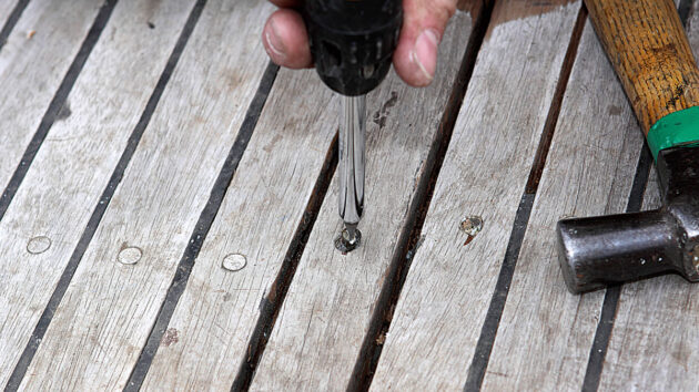 A man screwing a screw into a teak deck on a boat