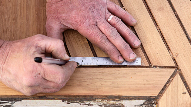 A man drawing a line on a plank on a teak deck of a boat