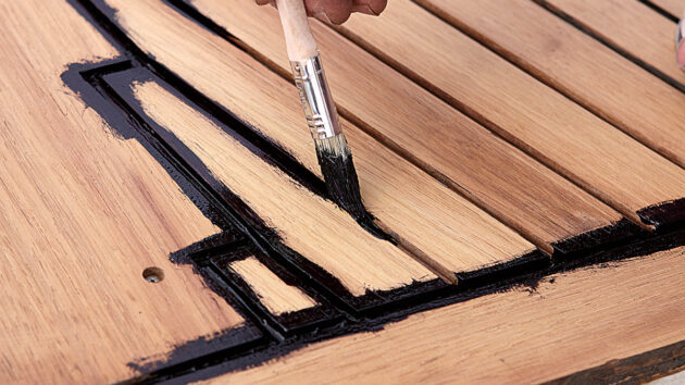 a man using a paintbrush to apply primer to a teak deck