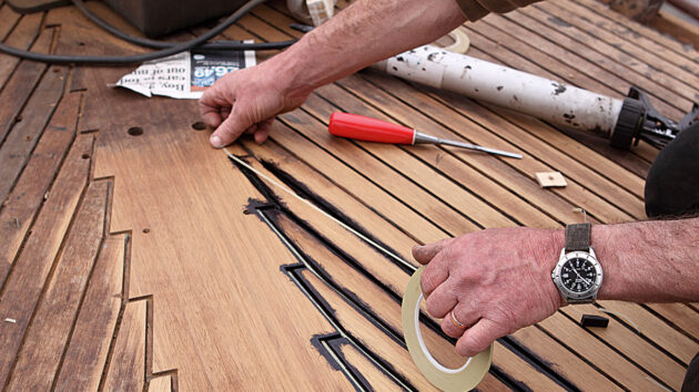 a man using tape on a teak deck on a boat