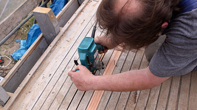 A man wearing ear defenders using a router on a teak deck on a boat