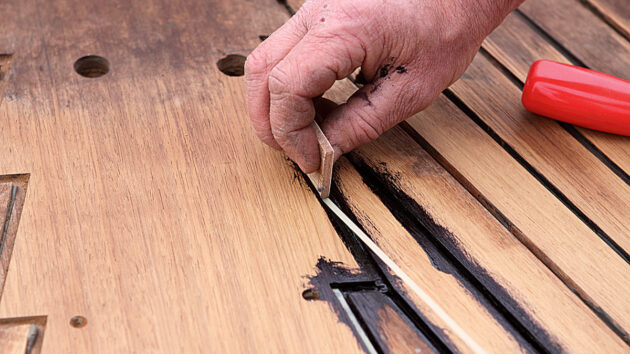 A man repairing a teak deck on a boat