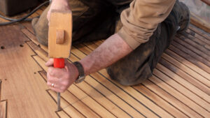 A man using a mallet and a chisel on a teak deck