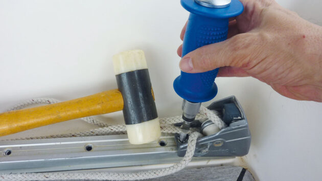 A man using a mallet and driver to remove a mainsheet track from a boat