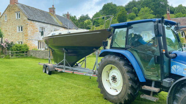 A Contessa 26 yacht without a mast on a trailer being towed by a tractor