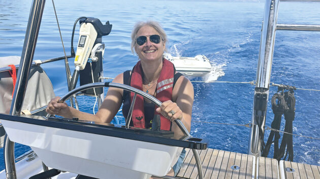 Smiling woman wearing a lifejacket at the helm of a yacht. Credit: Katy Stickland/Future Plc