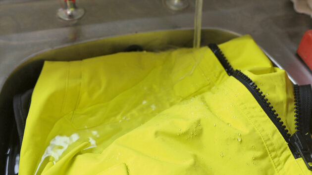 Rinsing saltwater off the surface of waterproof sailing gear to remove any dirt or contaminants. Credit: Gill/gb.gillmarine.com