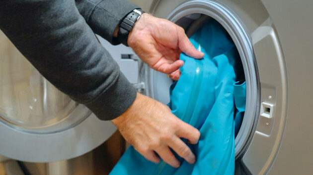 Man putting a zipped waterproof jacket into a washing machine. Credit: Gill/gb.gillmarine.com