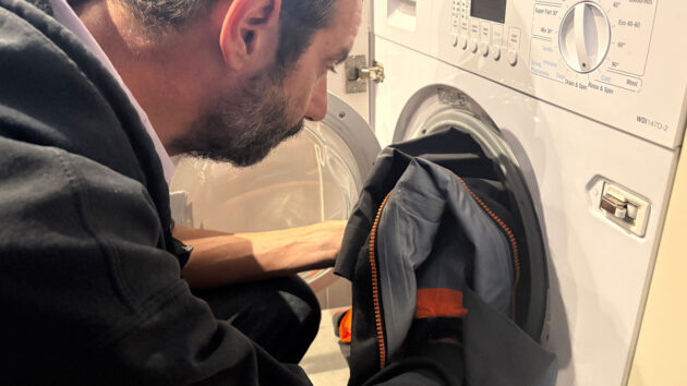 Man putting a waterproof sailing jacket in a domestic washing machine. Credit: Katy Stickland