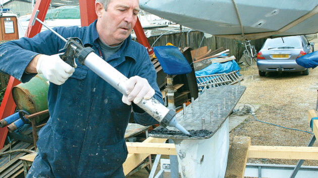 A man applying Sikaflex to the keel stub and keel bolts of a boat