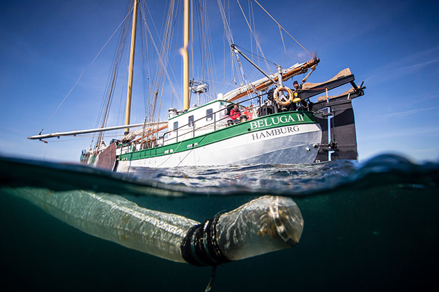 A can and a piece of plastic photographed under the water off Scotland with a green and white yacht behind it