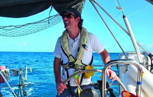 A man wearing a lifejacket helming a yacht