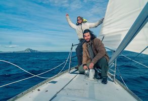 Two sailors on the deck of their yacht rounding Cape Horn