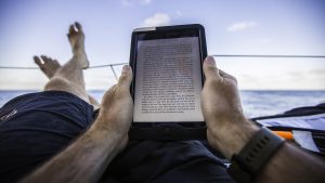 Books for sailors - a sailor reading a kindle on the deck of a boat