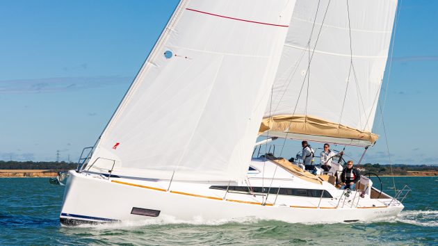 A Salona 46 with white sails sailing in the Solent under a blue sky with three people onboard