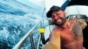 Double amputee single handed sailor Dustin Reynolds on his boat as it sails under a blue sky