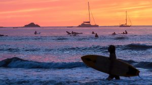 Surfers in Costa Rica with a sailing boat in the background as the sun sets