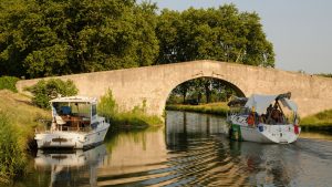 A yacht with no mast about to go under a bridge while canal cruising in France