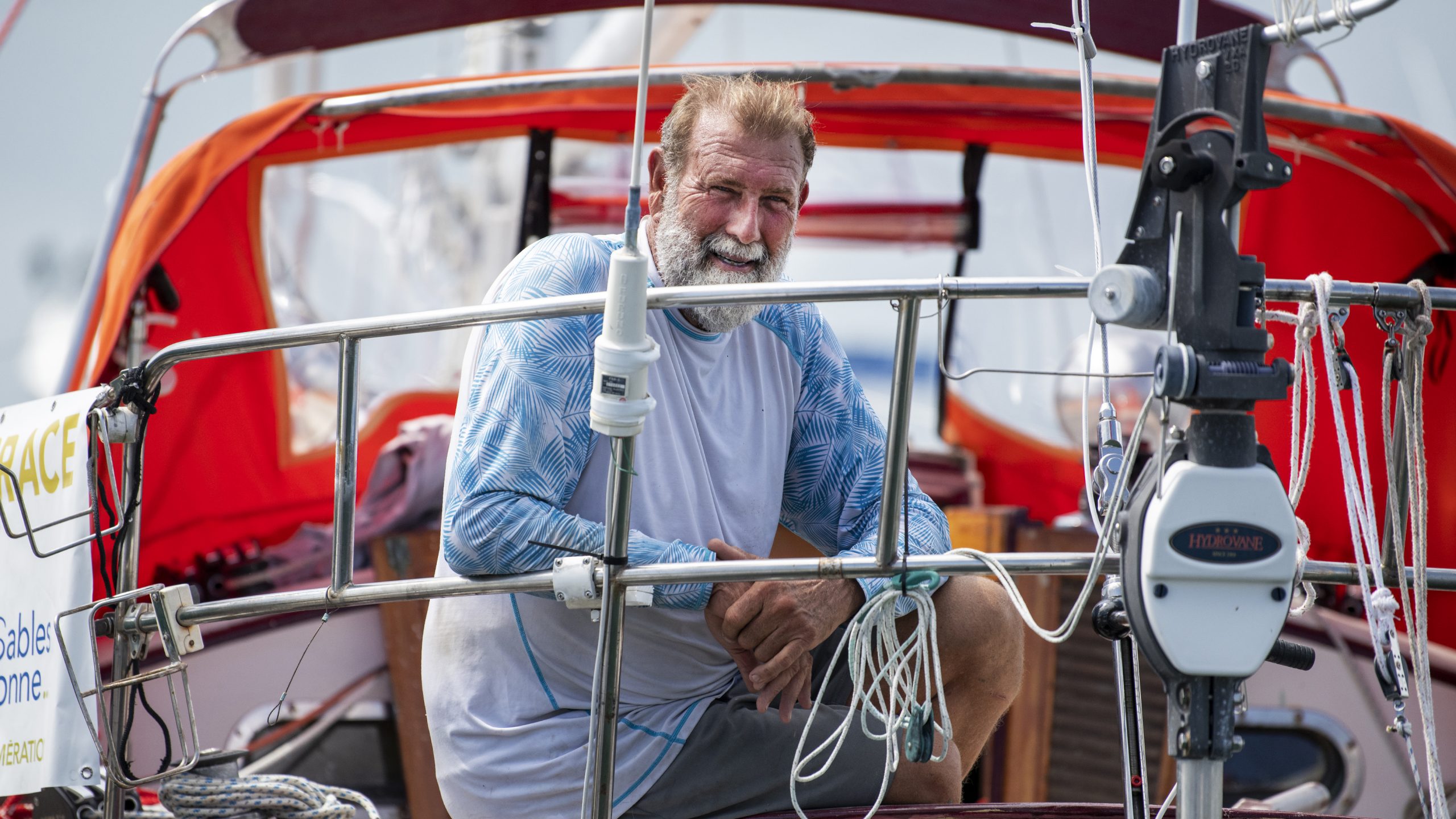 A man with a white beard wearing a blue and white t-shirt on the deck of a boat